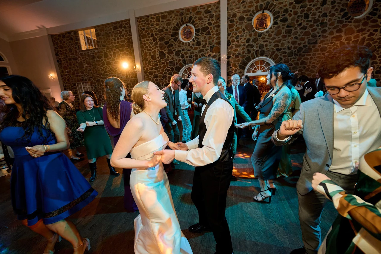 Abigail and Corey laughing together on the dance floor among their wedding guests