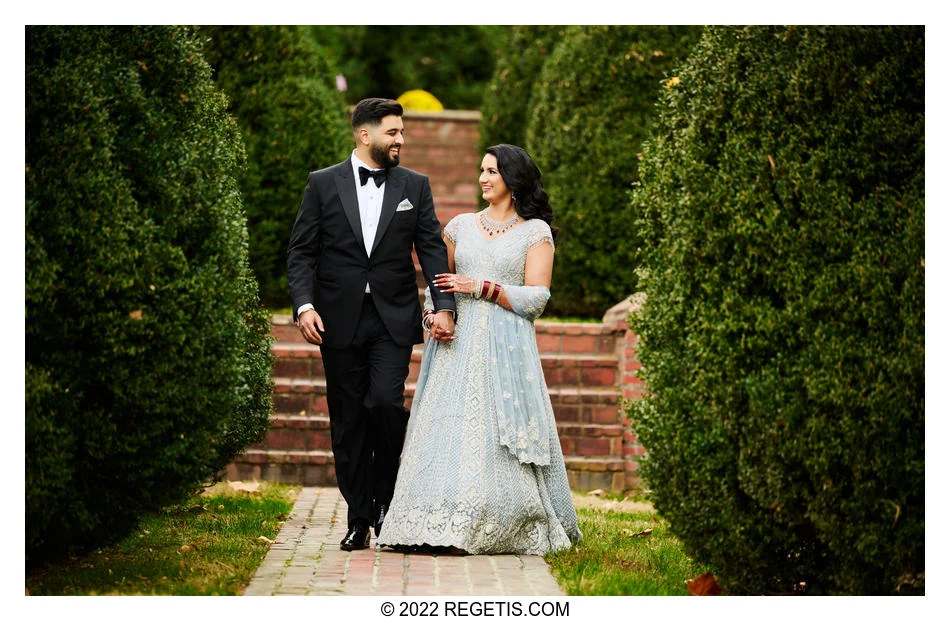 Akshay and Gurvina holding hands and smiling at one another between the garden hedges at Morven Park
