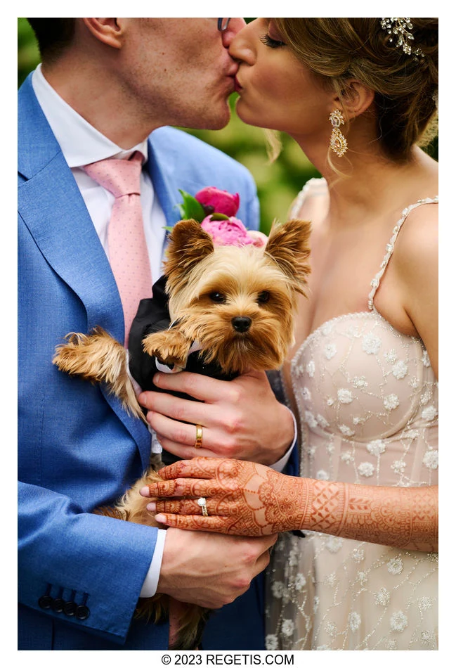 Arin and Anchal kissing while holding their small dog, with their wedding rings and her hennaed hands visible