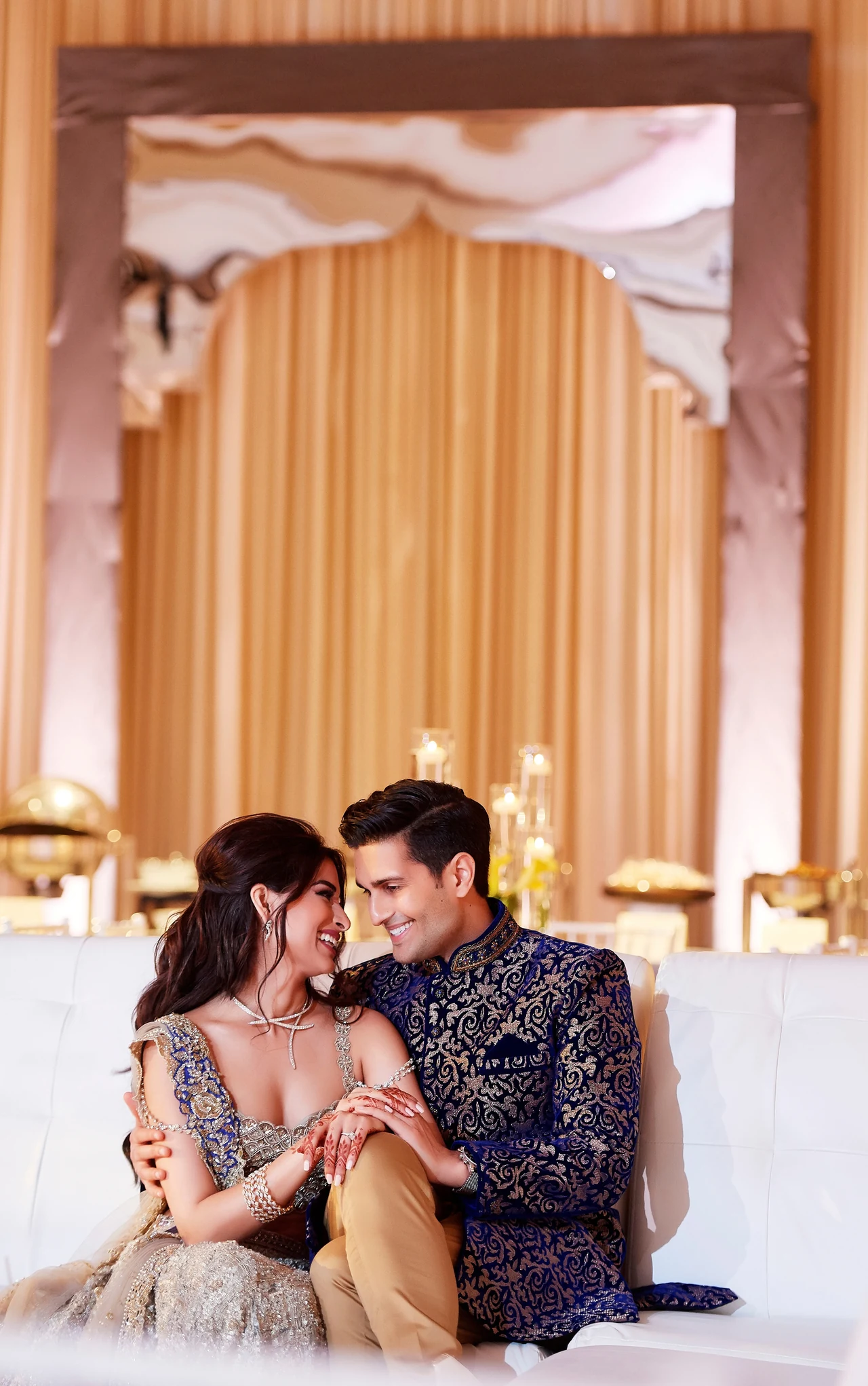 Ariana and Kunal seated close together, smiling and holding hands during their wedding celebrations