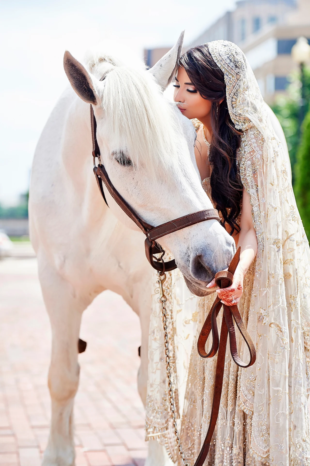 Ariana in ivory and gold wedding attire holding the reins of a white horse, her face close to its mane