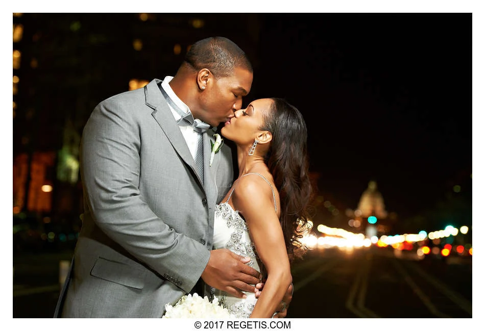 Chris and Monique sharing a kiss in their wedding attire with Washington, D.C. lights behind them