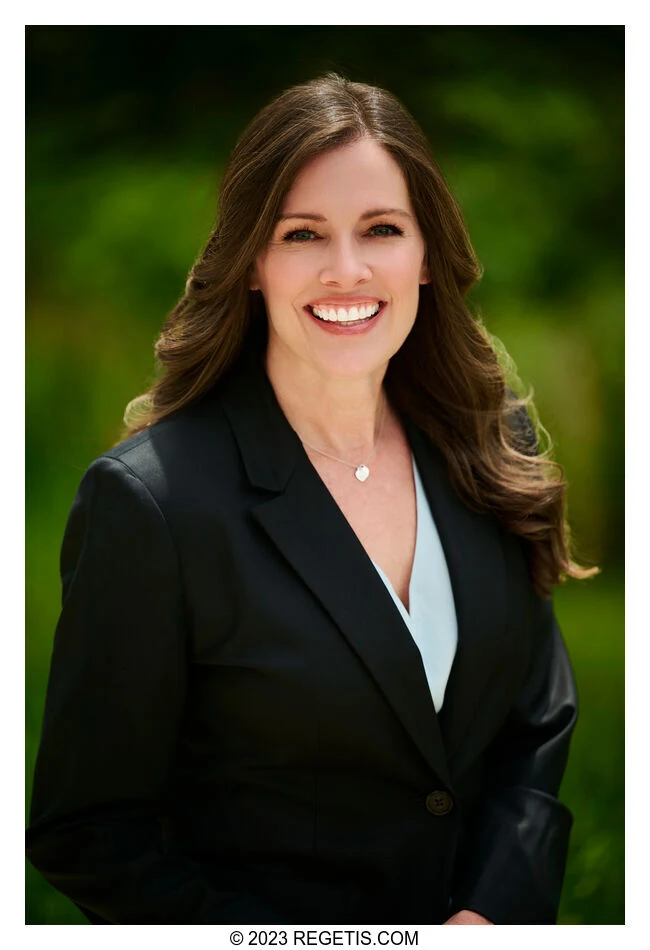 Gina Moore in a black blazer against a soft green outdoor background, photographed by The Regeti’s
