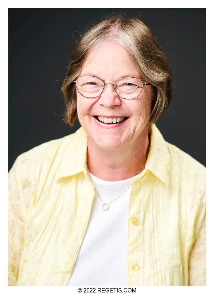 A smiling professional in a pale-yellow shirt photographed against a charcoal backdrop by The Regeti’s