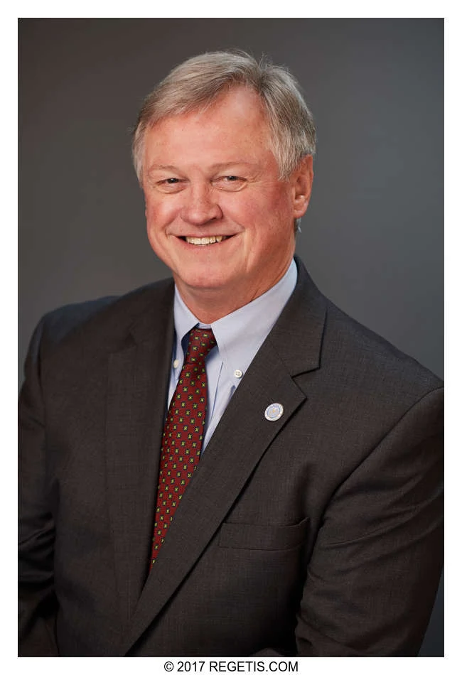 A Walker Jones attorney in a dark suit and red tie, photographed against a charcoal-gray backdrop by The Regeti’s