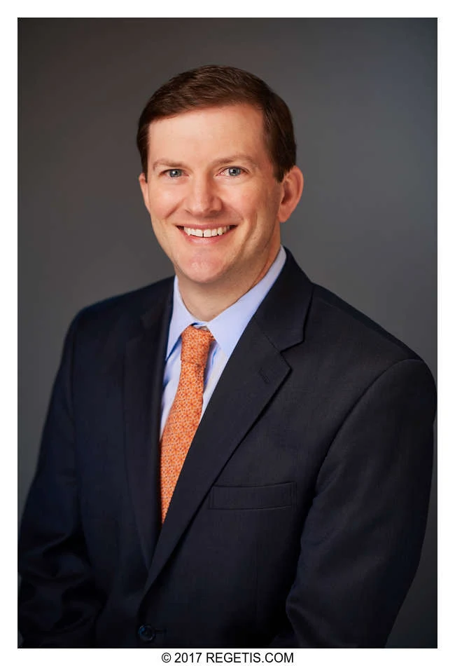 A Walker Jones attorney in a navy suit and orange tie, photographed against a charcoal-gray backdrop by The Regeti’s