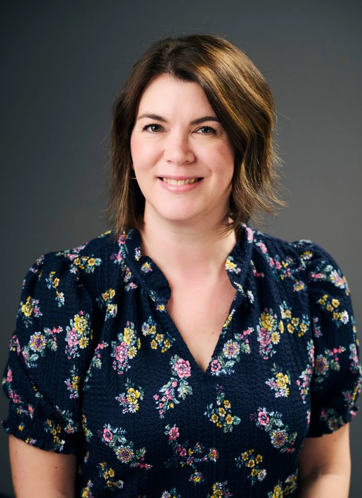 A PATH professional in a navy floral blouse, photographed against a charcoal studio backdrop by The Regeti’s