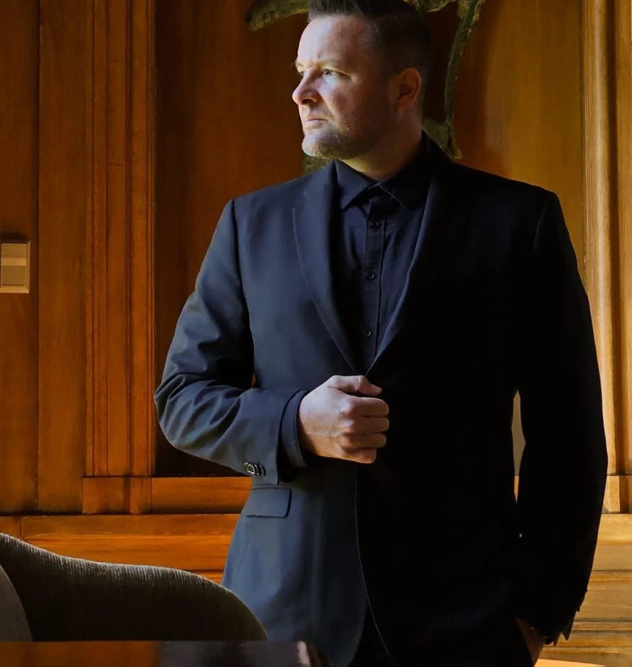 Diego Stuart in a dark suit beside a wood-paneled window