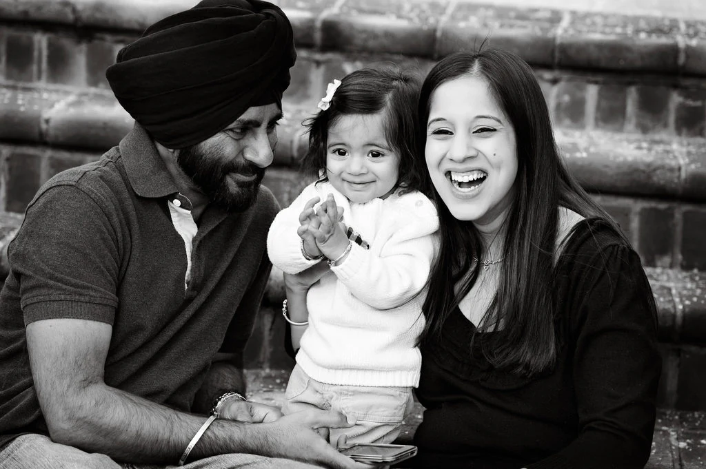 Two parents sharing a joyful moment with their young child in a black-and-white family portrait by The Regeti’s