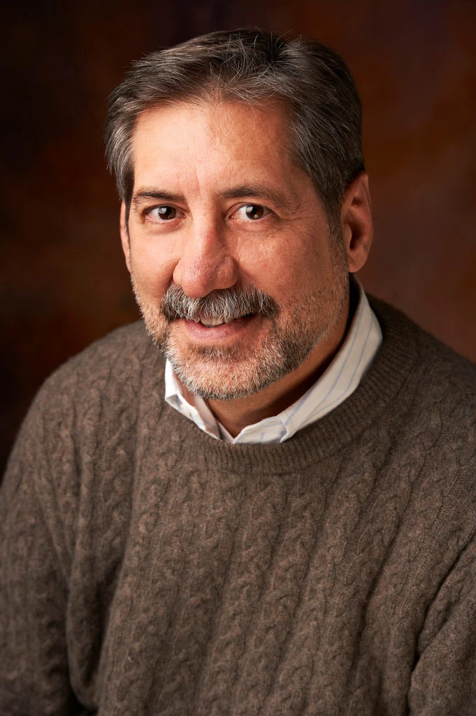 An author in a brown sweater, photographed in warm studio light by The Regeti’s