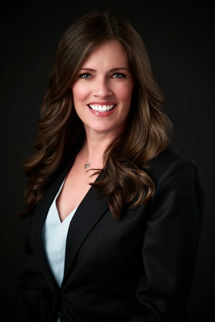 Gina smiling in a black blazer in a professional headshot by The Regeti’s