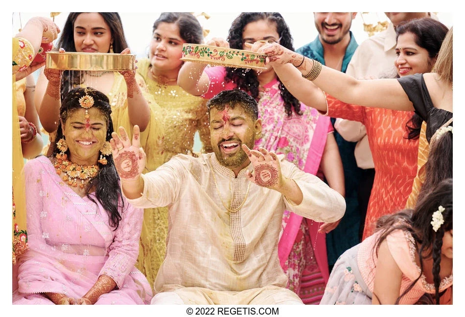 Jahnavi and Samir smiling as loved ones pour water through ceremonial trays at their Haldi
