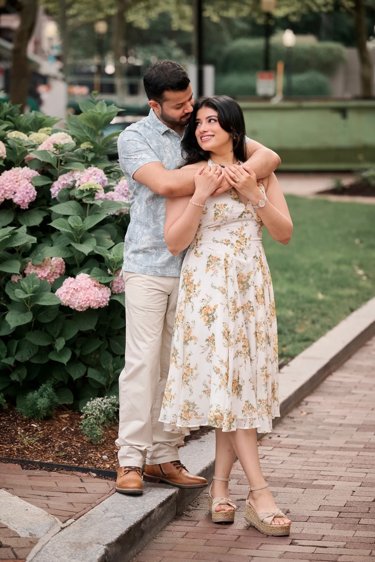Durgesh embracing Nikitaa beside pink hydrangeas as she smiles up at him