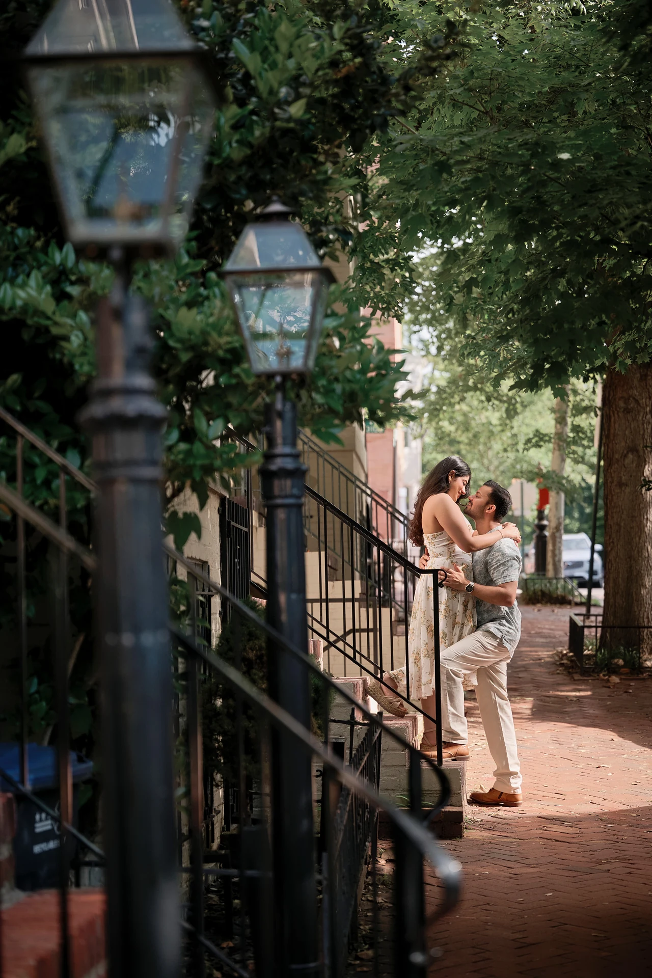 Nikitaa and Durgesh sharing a playful embrace on outdoor steps beneath leafy trees