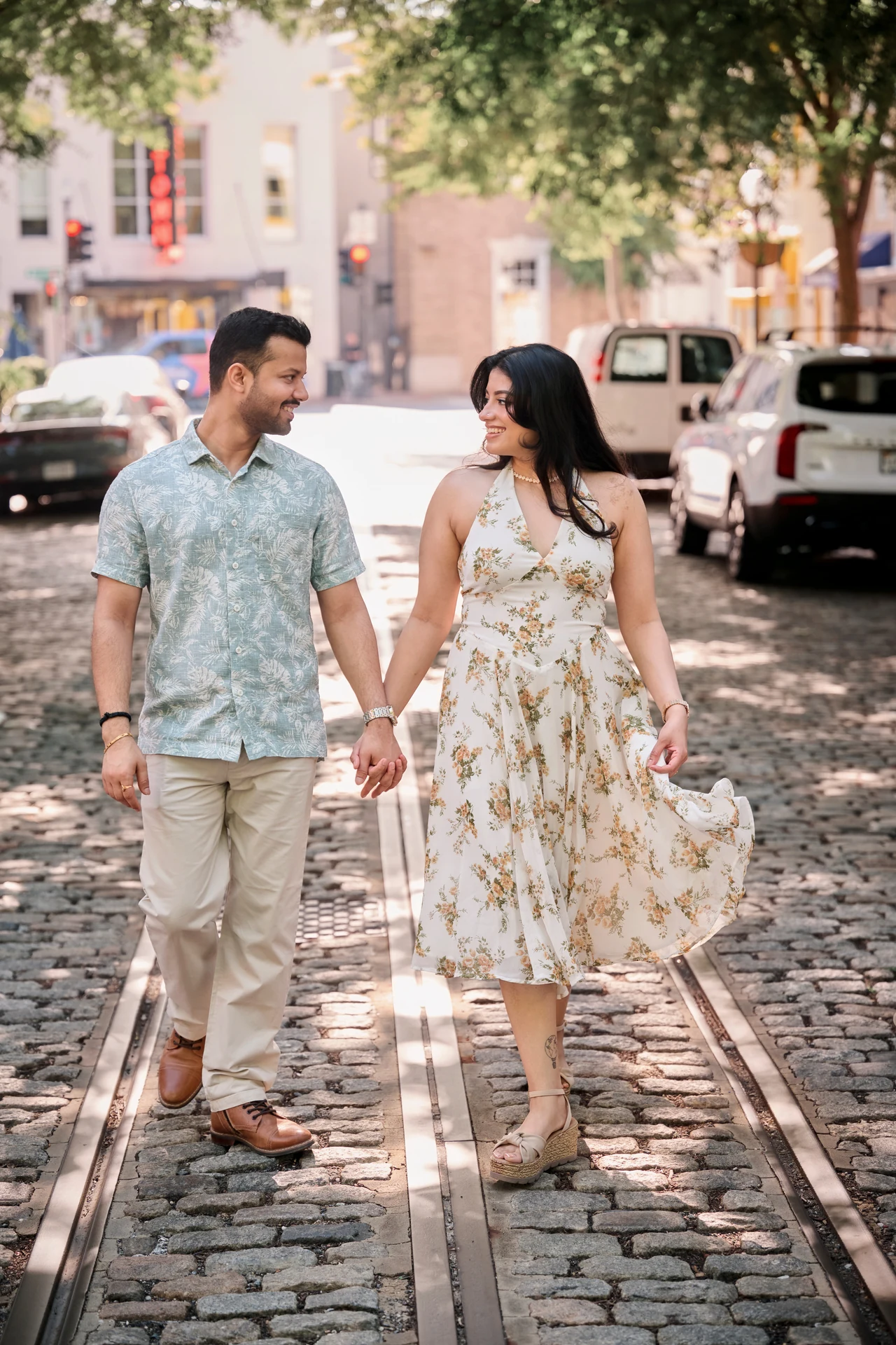 Nikitaa and Durgesh holding hands and smiling at each other as they walk along a cobblestone street