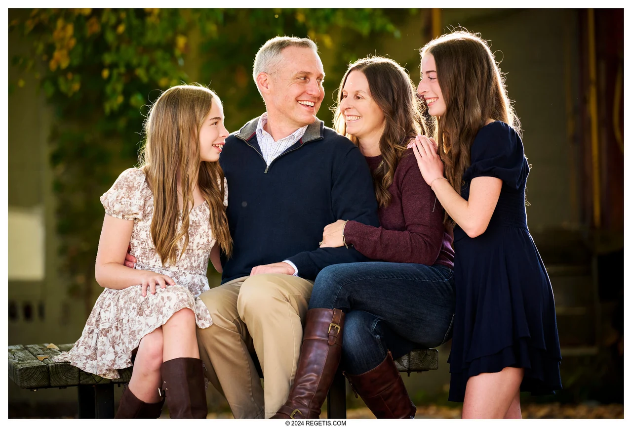 A family of four smiling toward one another in a warmly lit outdoor portrait in Warrenton, photographed by The Regeti’s