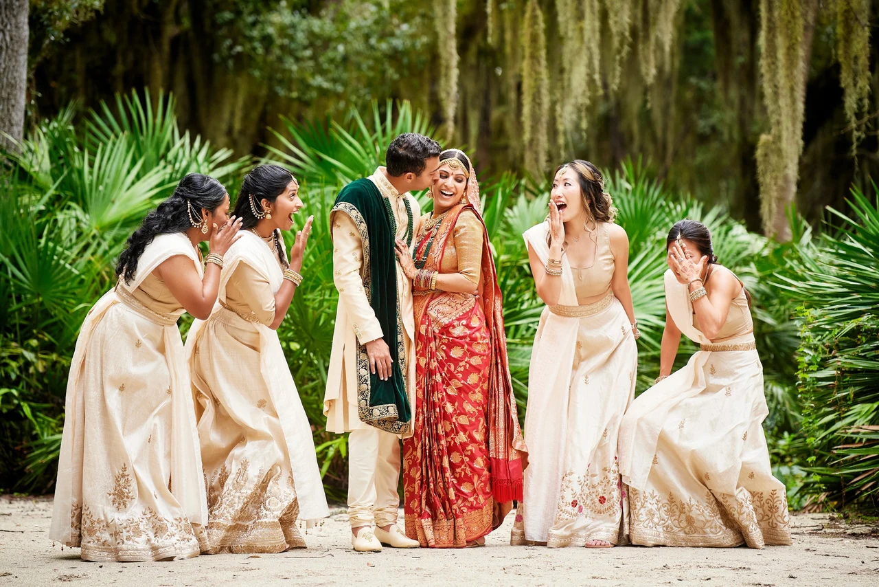 Arjun kissing Shruthi as she and her bridesmaids laugh beneath Spanish moss at their Amelia Island wedding